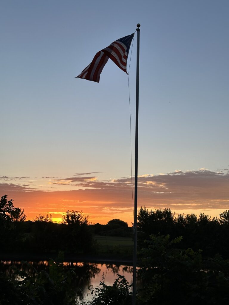 American flag on a flagpole silhouetted against a sunset over a Wisconsin pond